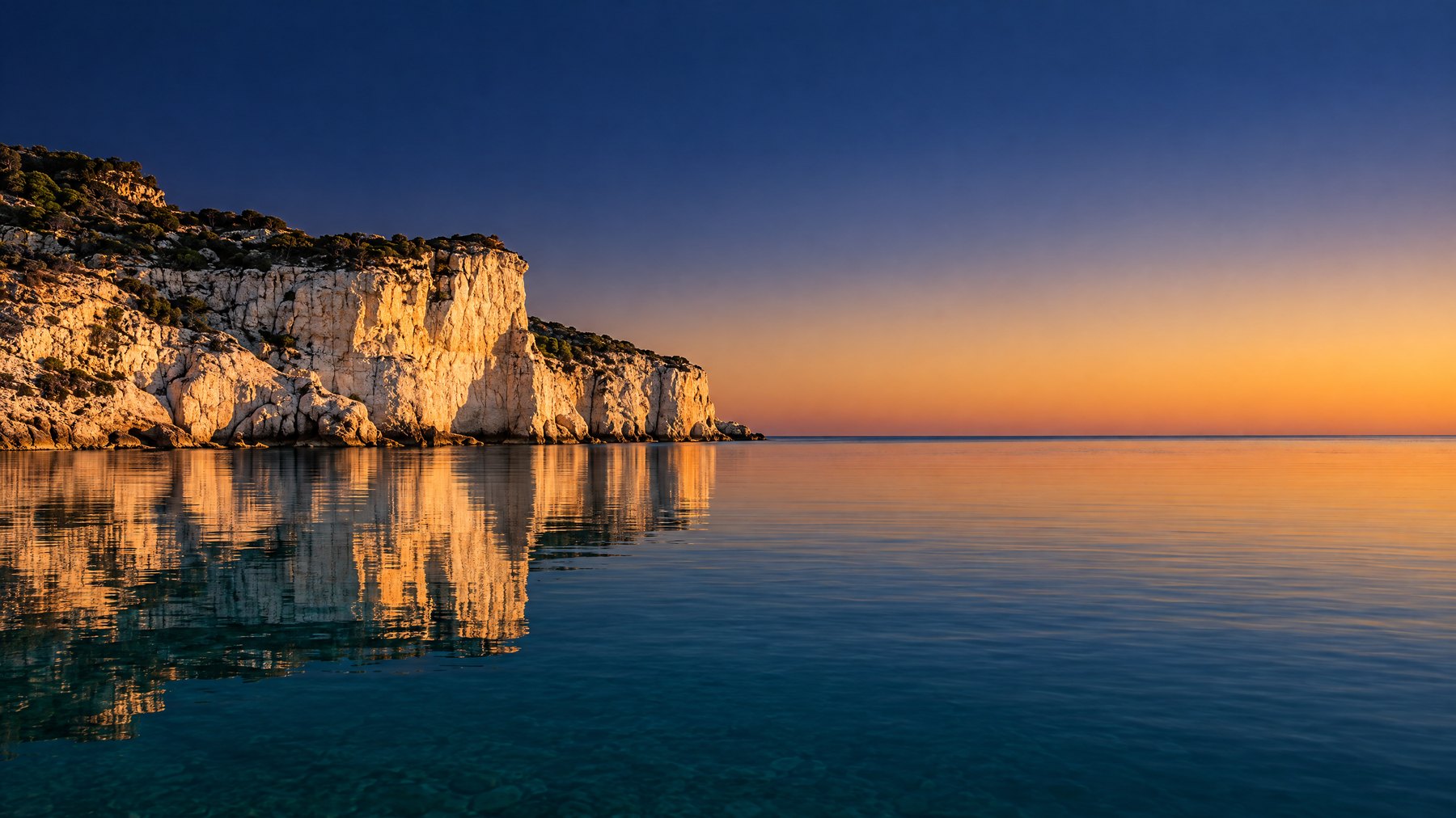 A warm Mediterranean coastline in late light, white cliffs above calm green water. The sea is the industry landscape every practice sits inside.